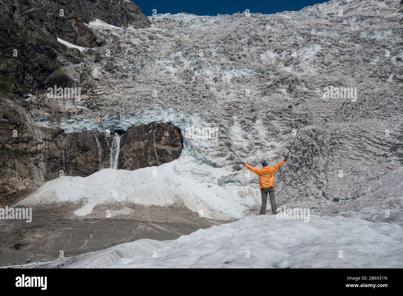Touristen, die mit orangefarbenem Windschutzschalter bekleidet sind, blicken auf den Adishi-Gletscher (auch Lardaad genannt). Der Tropfen dieses Eisfalles beträgt mehr als 1000 m. Stockfoto