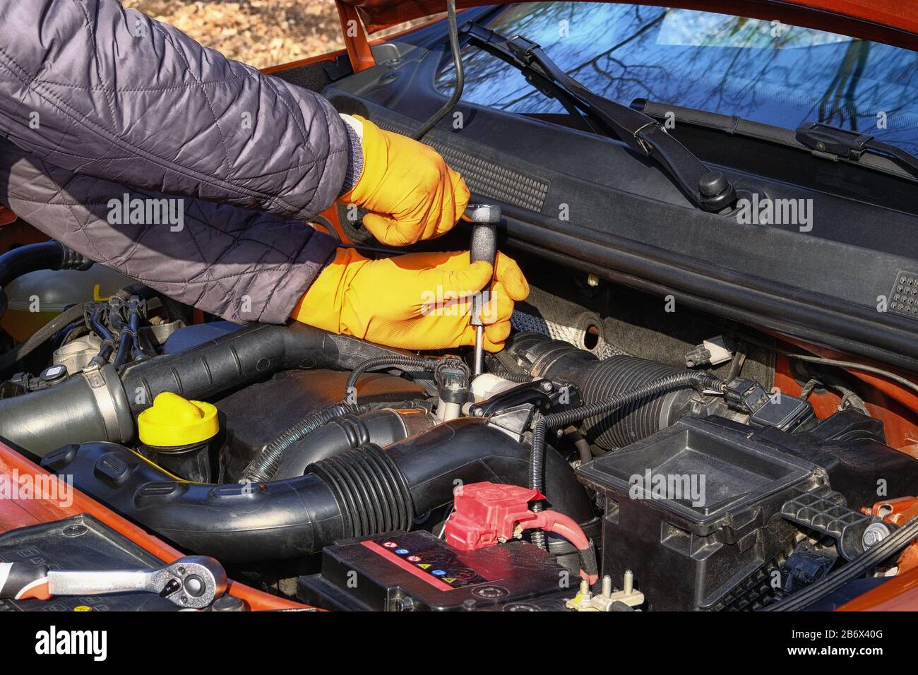 Fahrzeugwartung und Reparaturkonzept. Die Hände des Fahrers in orangefarbenen Gummihandschuhen prüfen das Fahrzeug mit den Werkzeugen, öffnen Sie die Haube. Auto und Transport, Nahaufnahme Stockfoto
