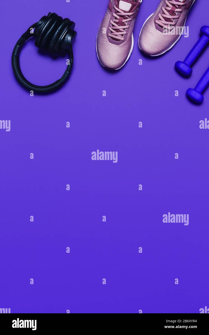 Sportwohnung mit Turnschuhen, Hanteln und Kopfhörern auf blauem Hintergrund. Vertikales Bild. Stockfoto