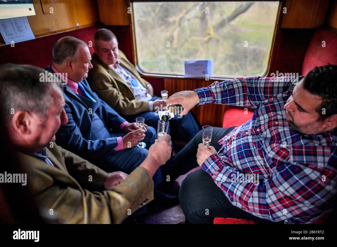 Racegoers gießen Champagne an Bord einer Oldtimer-Eisenbahnwaggon am Bahnhof Toddington in Gloucestershire, wo die Leute einen Dampfzugdienst zu Cheltenham Rennen, die während des Festivals laufen, fangen. Stockfoto
