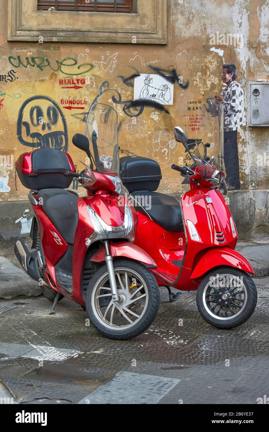 FLORENZ ITALIEN ROTES MOTORRAD UND ROTER VESPA-ROLLER VOR EINER WAND MIT GRAFFITI-KUNST Stockfoto