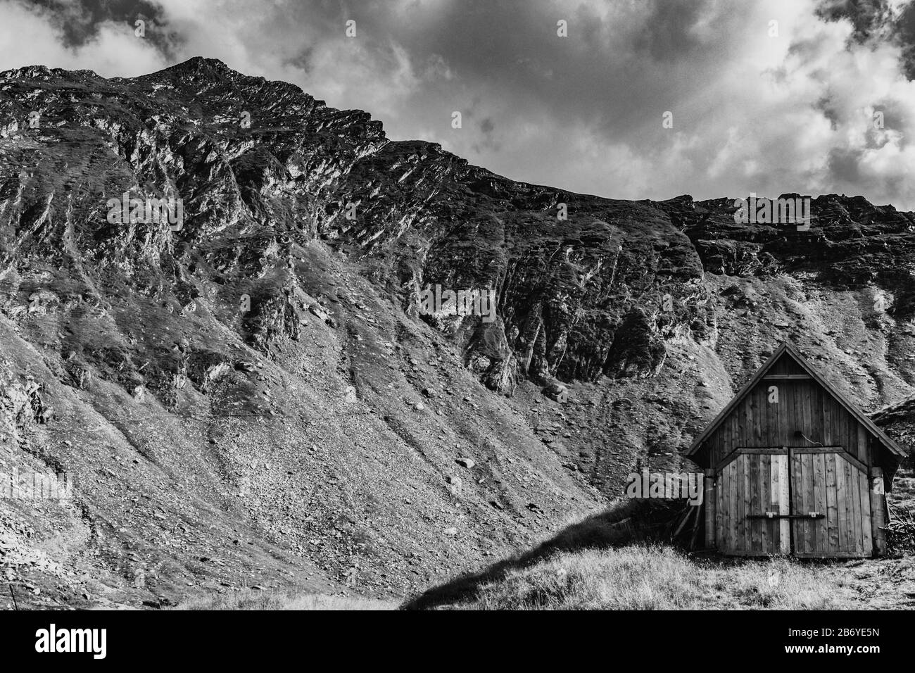 Schwarz-weiße Zusammensetzung der Scheune in einer Bergkulisse mit Berg im Hintergrund und verpufften Wolken darüber Stockfoto