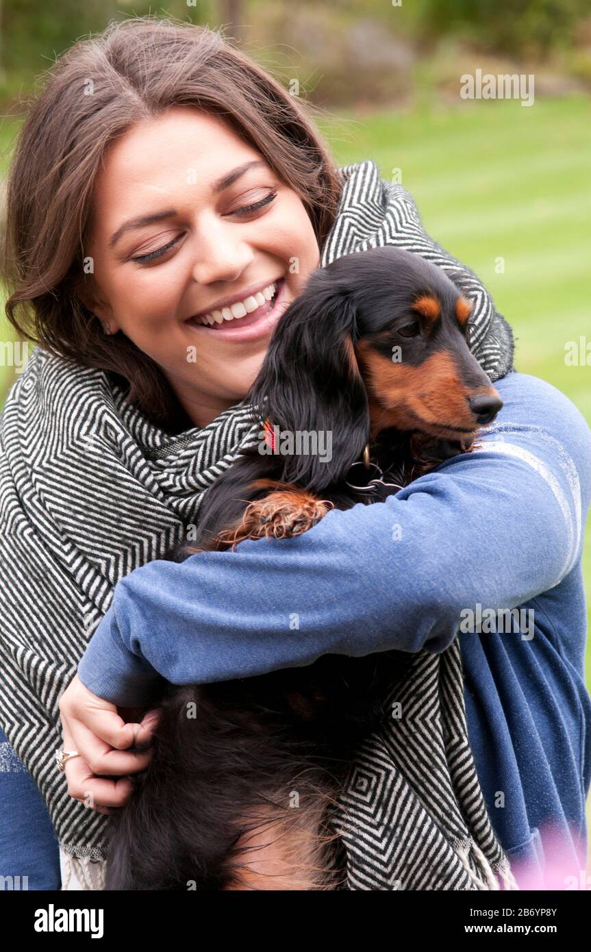 Fröhliche junge Frau, die ihren kleinen langhaarigen Dachsund kuschelt Stockfoto