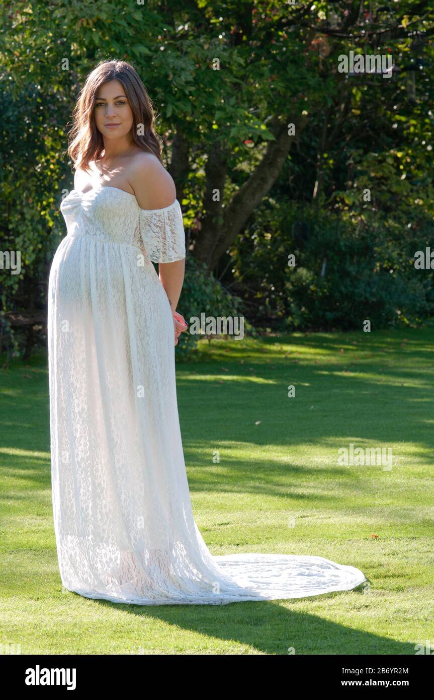 Schöne schwangere junge Frau, die ein langes weißes Kleid trägt und ihr  Baby streichelt Stockfotografie - Alamy