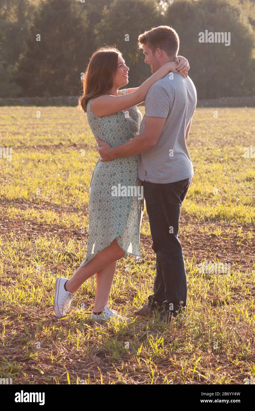 Schwangere junge Frau mit ihrem Partner, die mit den Armen um sich herum auf einem Feld steht Stockfoto