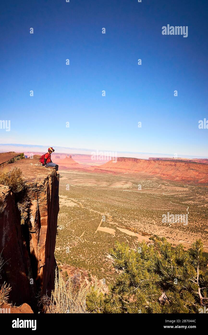 Ein Mann liegt am Rande einer großen Klippe mit Blick auf Monument Valley. Stockfoto