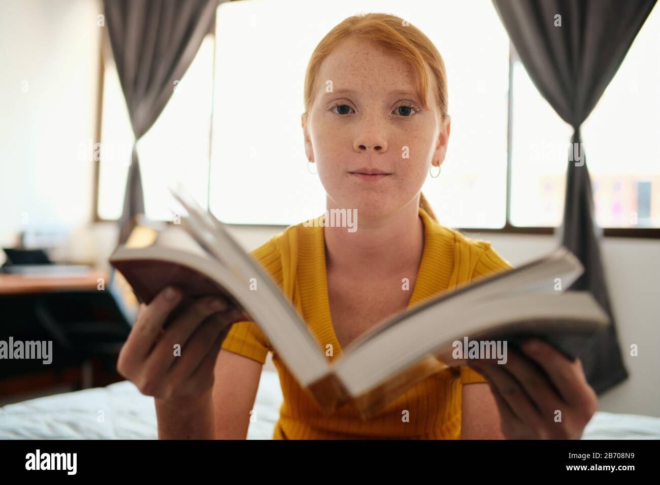 Young Redhead Girl Studieren Und Zeigen Book To Camera Stockfoto