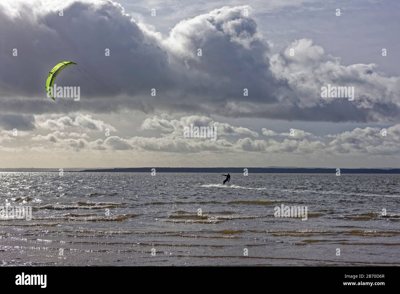 Ein Kite Surfer in der Tay Estuary an der Ostküste Schottlands surft parallel zur Küstenlinie an einem Windy Day im März. Stockfoto
