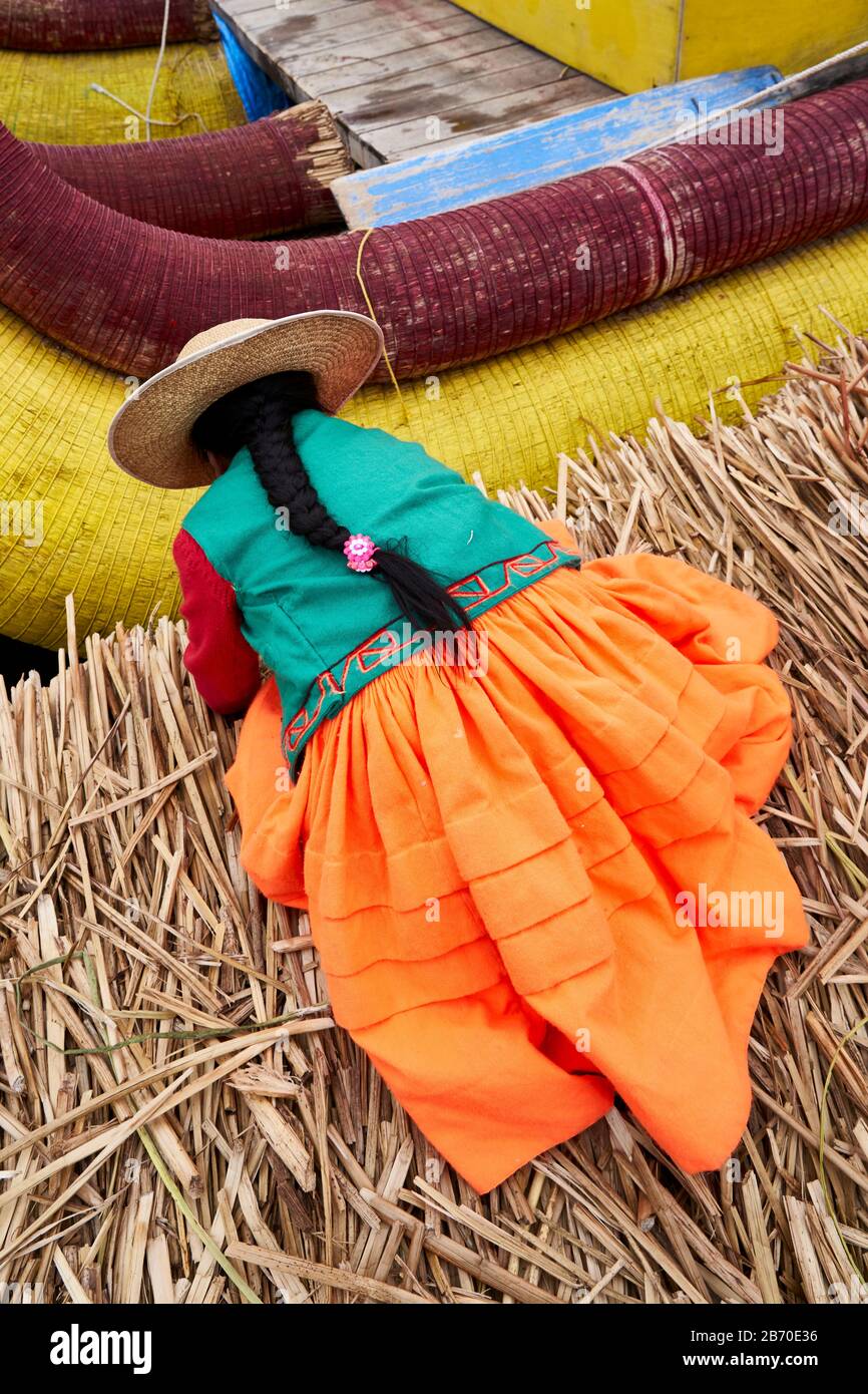 Einheimische Frau, die auf der schwimmenden Insel Uros, Lago Titicaca, Peru, ein Schilfboot anschnürt Stockfoto