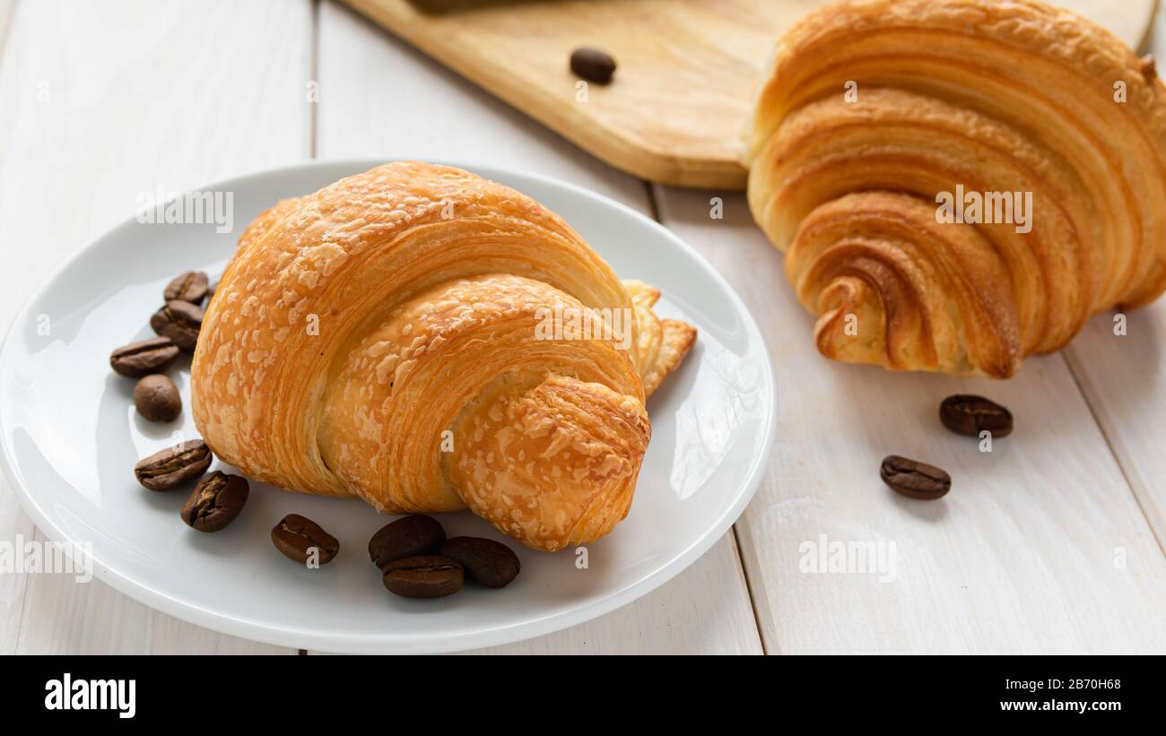 Zwei Croissants und Kaffeekörner auf einem weißen Holztisch Stockfoto