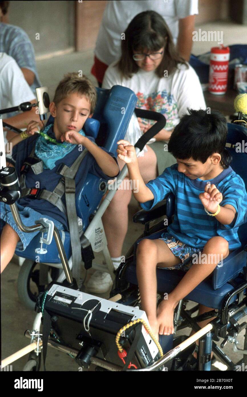 Hunt Texas USA: Der 7-jährige nonverbale Junge (rechts) mit zerebraler Lähmung kommuniziert mit seinem großen Zeh, indem er in einem Sommerlager für Kinder mit sprach- und Sprachbehinderungen Tasten auf einem Liberator-Gerät drückt. HERR ©Bob Daemmrich Stockfoto