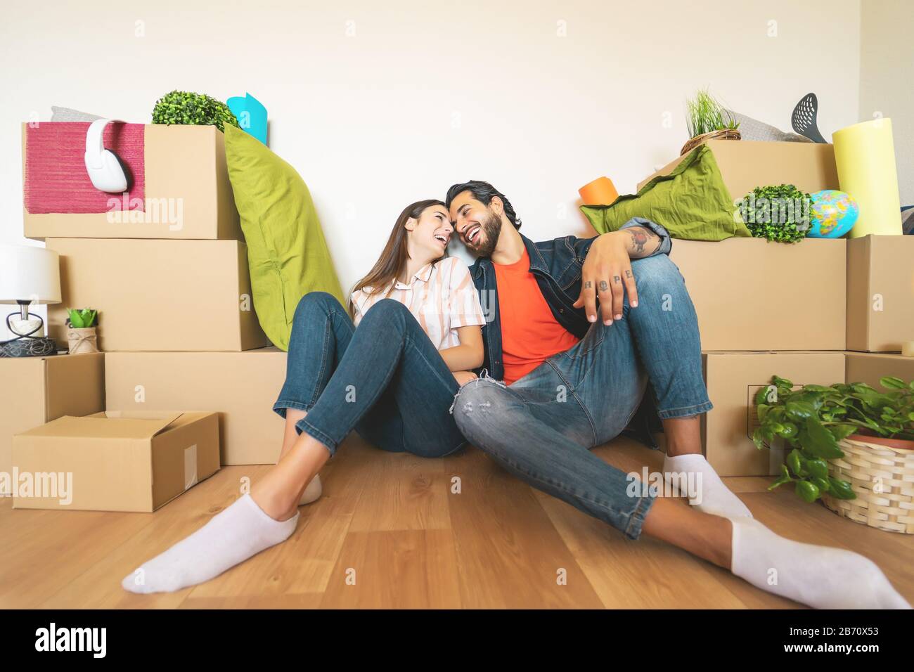 Glückliches junges Paar, das zum ersten Mal nach Hause zieht - Mann und Frau haben Spaß beim Auspacken der Kartonschachtel im neuen Haus Stockfoto