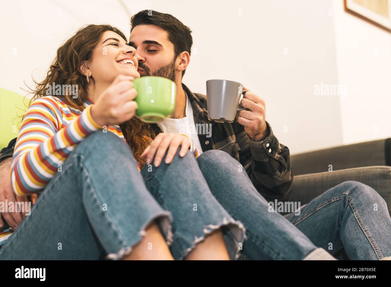 Junges Paar trinkt Kaffeetasse auf dem Boden neben dem Sofa - glückliche Liebhaber haben zu Hause zarte Momente zusammen Stockfoto