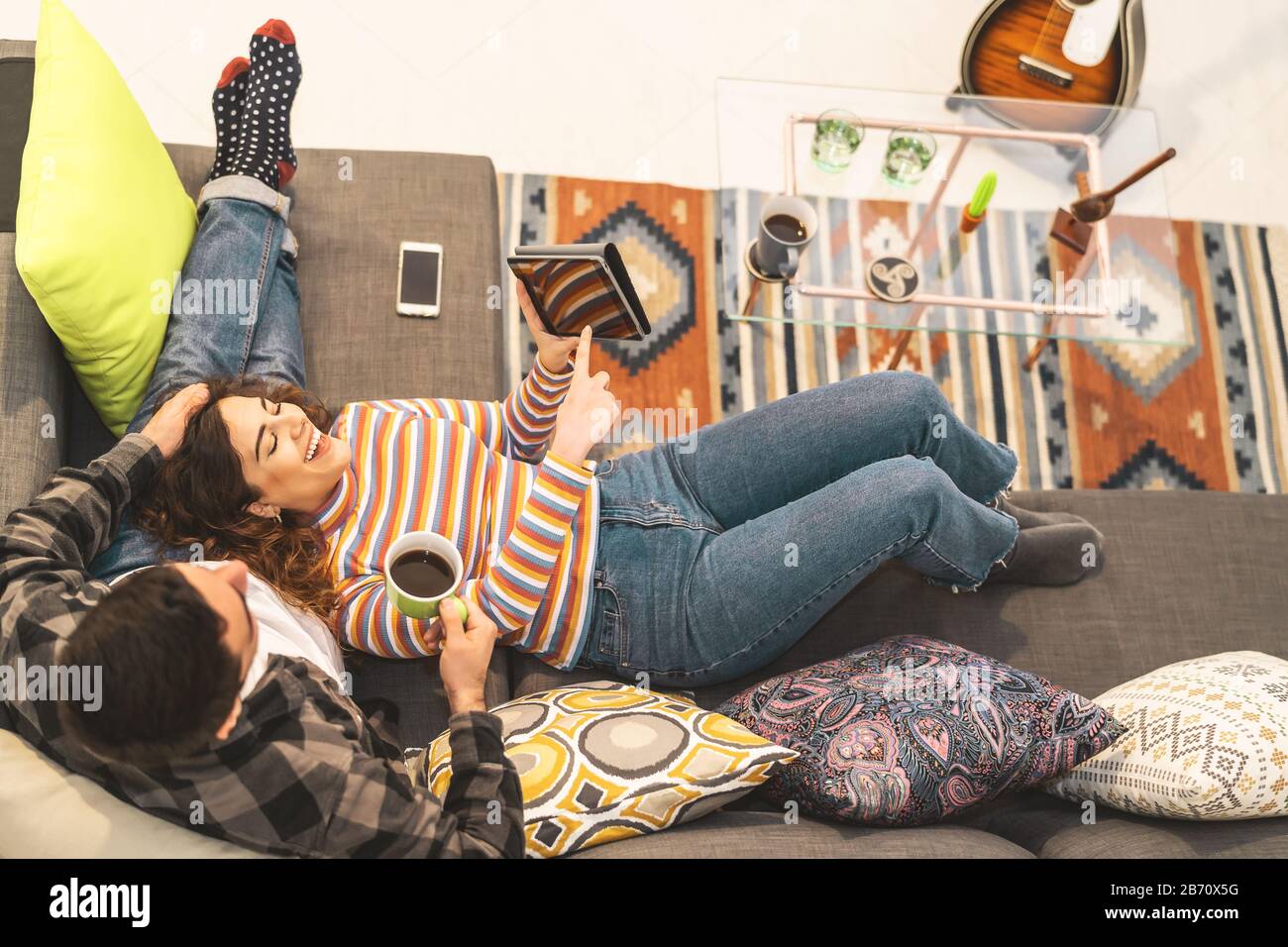 Glückliches Paar, das sich zu Hause auf dem Sofa entspannen kann - junge romantische Liebhaber haben Spaß mit neuen Technologiegeräten für Trends Stockfoto