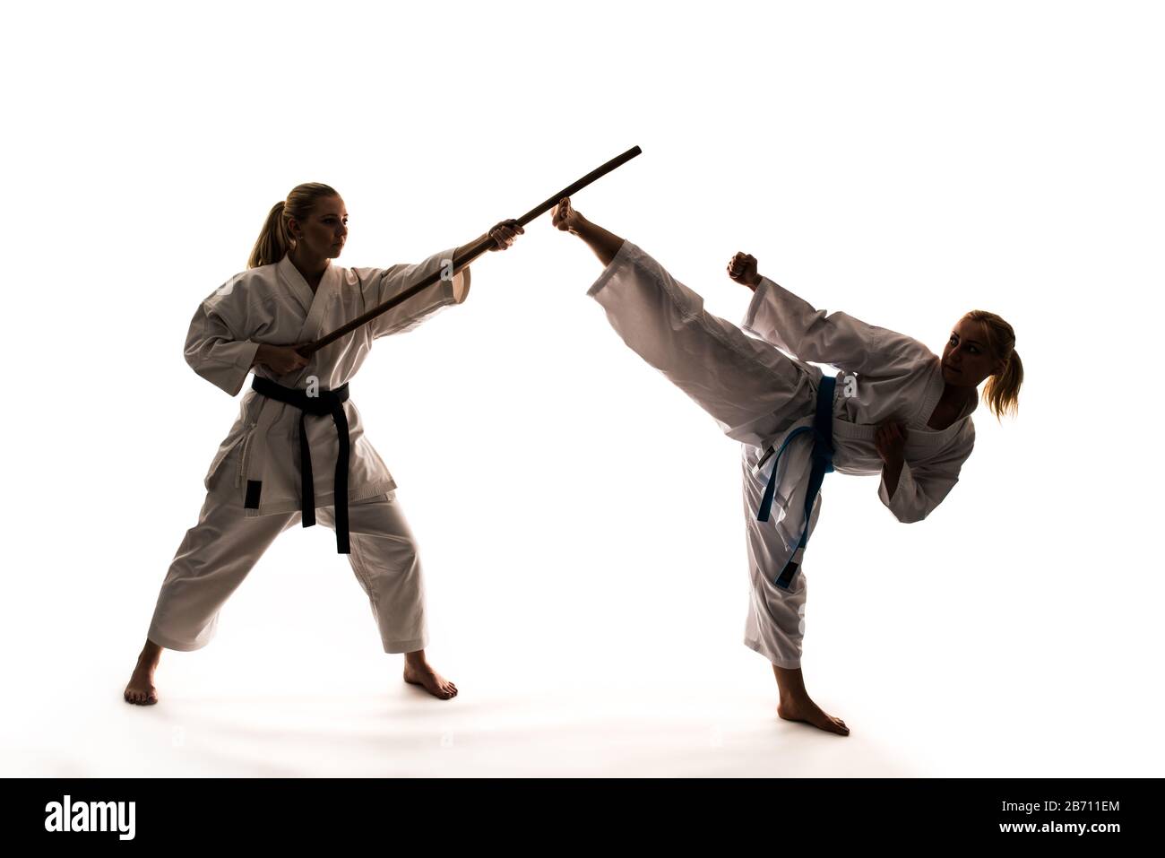 Training von zwei Mädchen in weißen Kimonos mit Sportgeräten und Karate-Ständer. Isoliert auf weißem Hintergrund Stockfoto