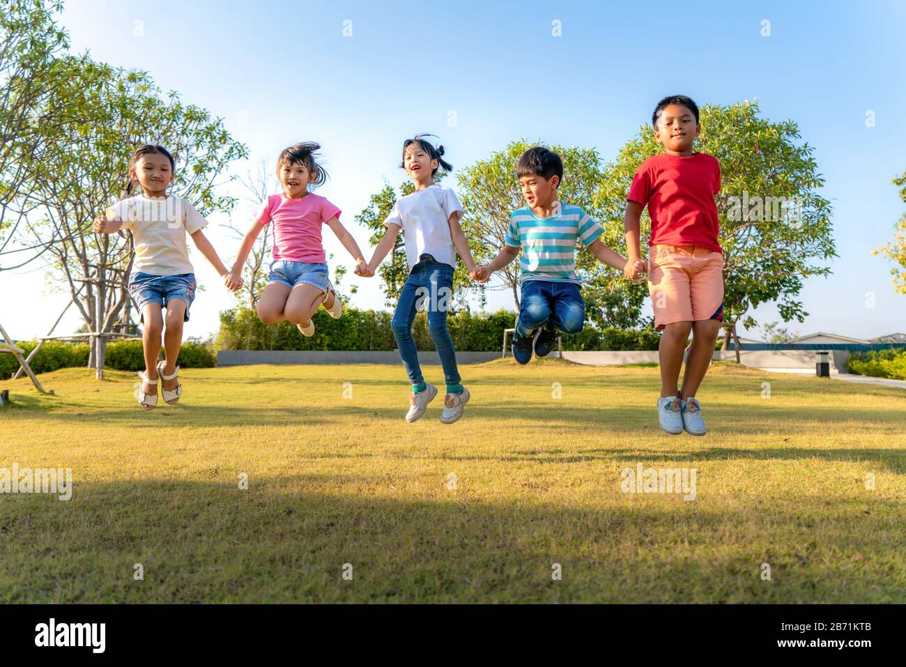 Große Gruppe von fröhlichen asiatischen Kindergartenfreunden, die an einem sonnigen Tag in legeren Kleidungsstücken in der Stadt p die Hände beim Spielen und Springen zusammenhalten Stockfoto