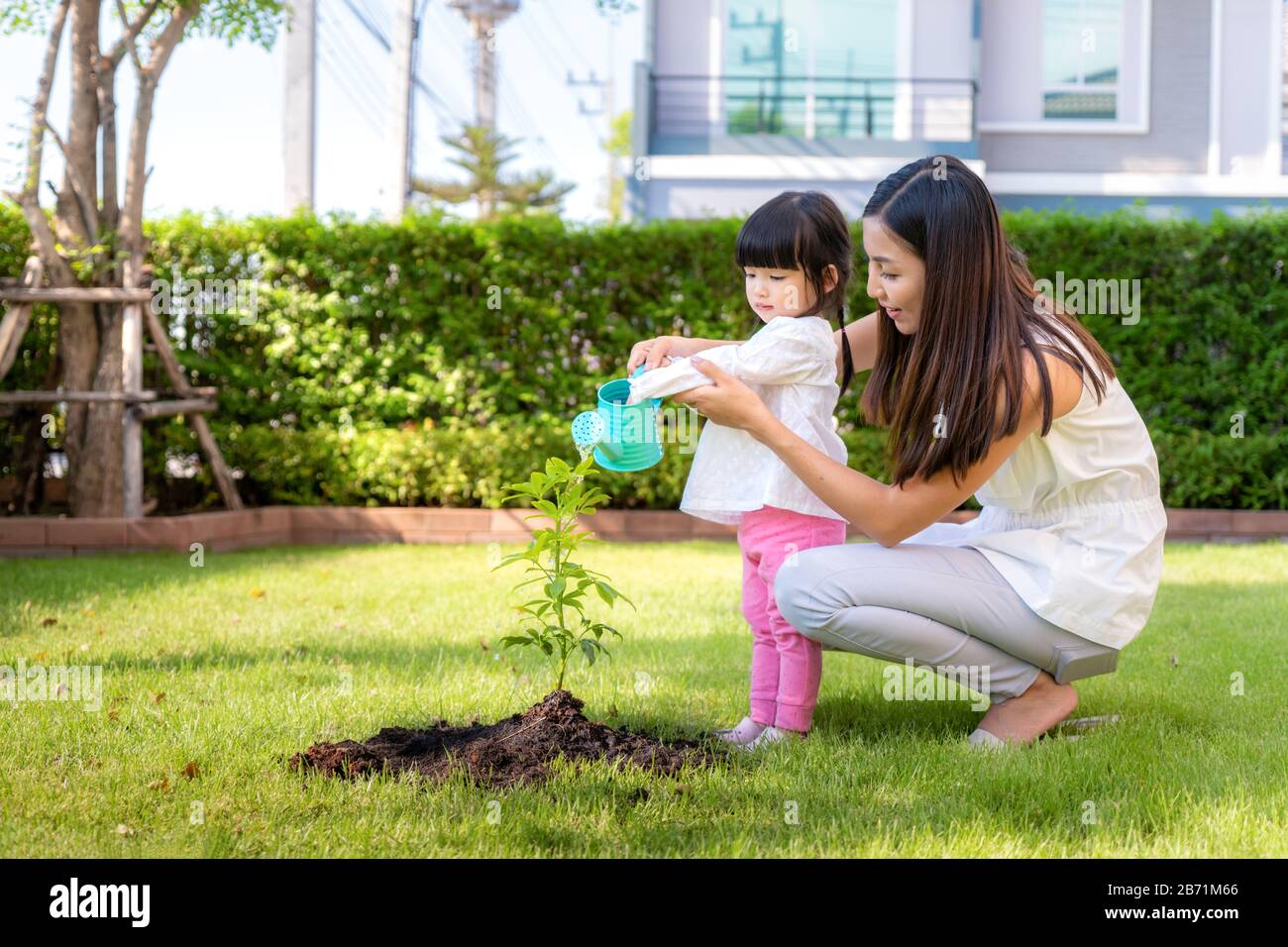Asiatische Familienmutter und Kindertochter sättern Baum und wässern im Freien im Naturfrühling, um das Wachstum der globalen Erwärmung zu reduzieren und vorsichtig zu sein Stockfoto