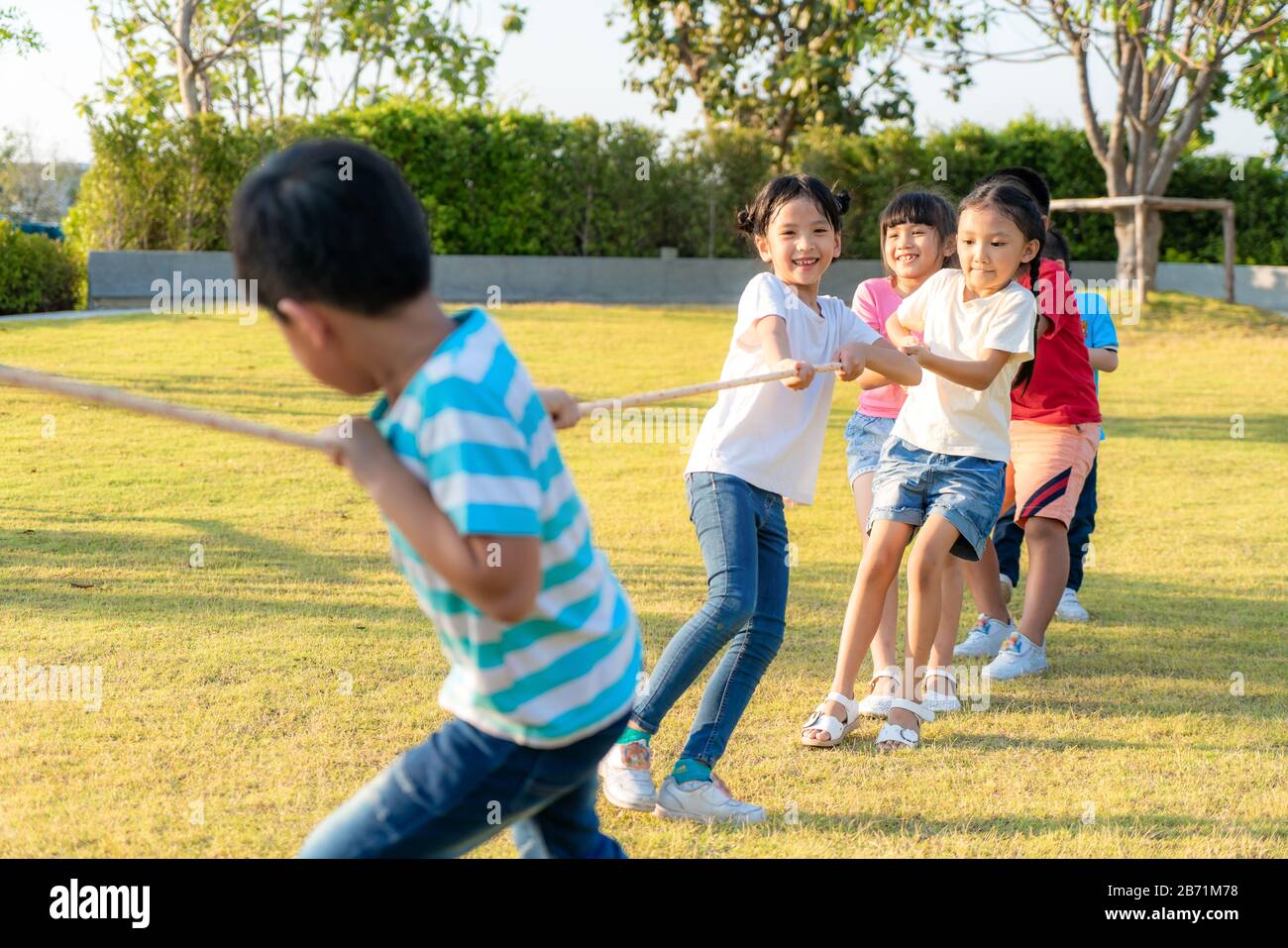 Gruppe glücklicher asiatischer Kleinkinder, die im Sommer auf dem Spielplatz im Stadtpark Krieg spielen oder Seiltogerther nach draußen ziehen. Kinder und Freizeit c Stockfoto