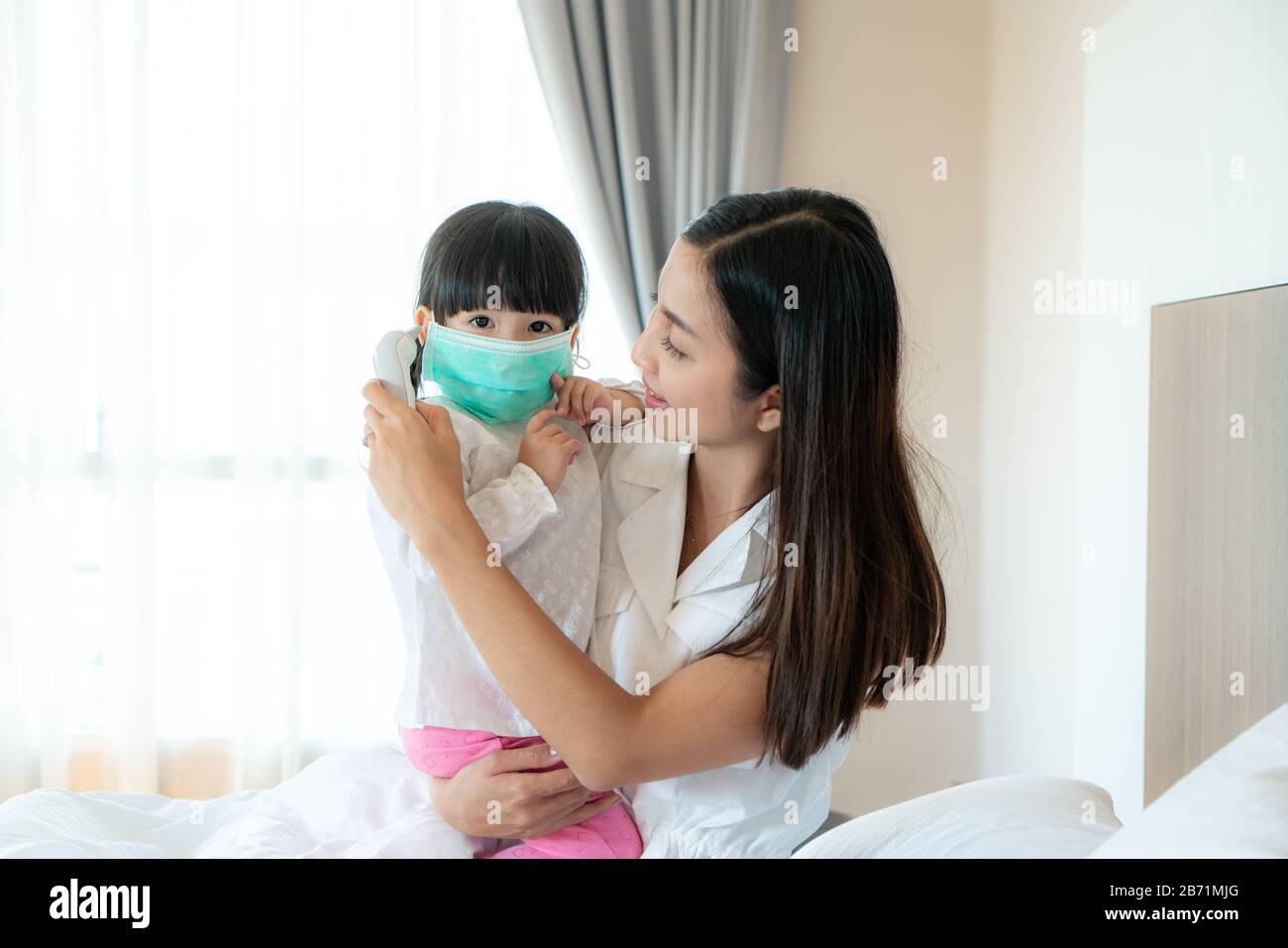 Asiatische junge Mutter, die die Temperatur ihrer kranken kleinen Tochter überprüft, fühlt sich wie Fieber oder Grippe im Schlafzimmer zuhause an. Bilder von Menschen, die sich fühlen Stockfoto