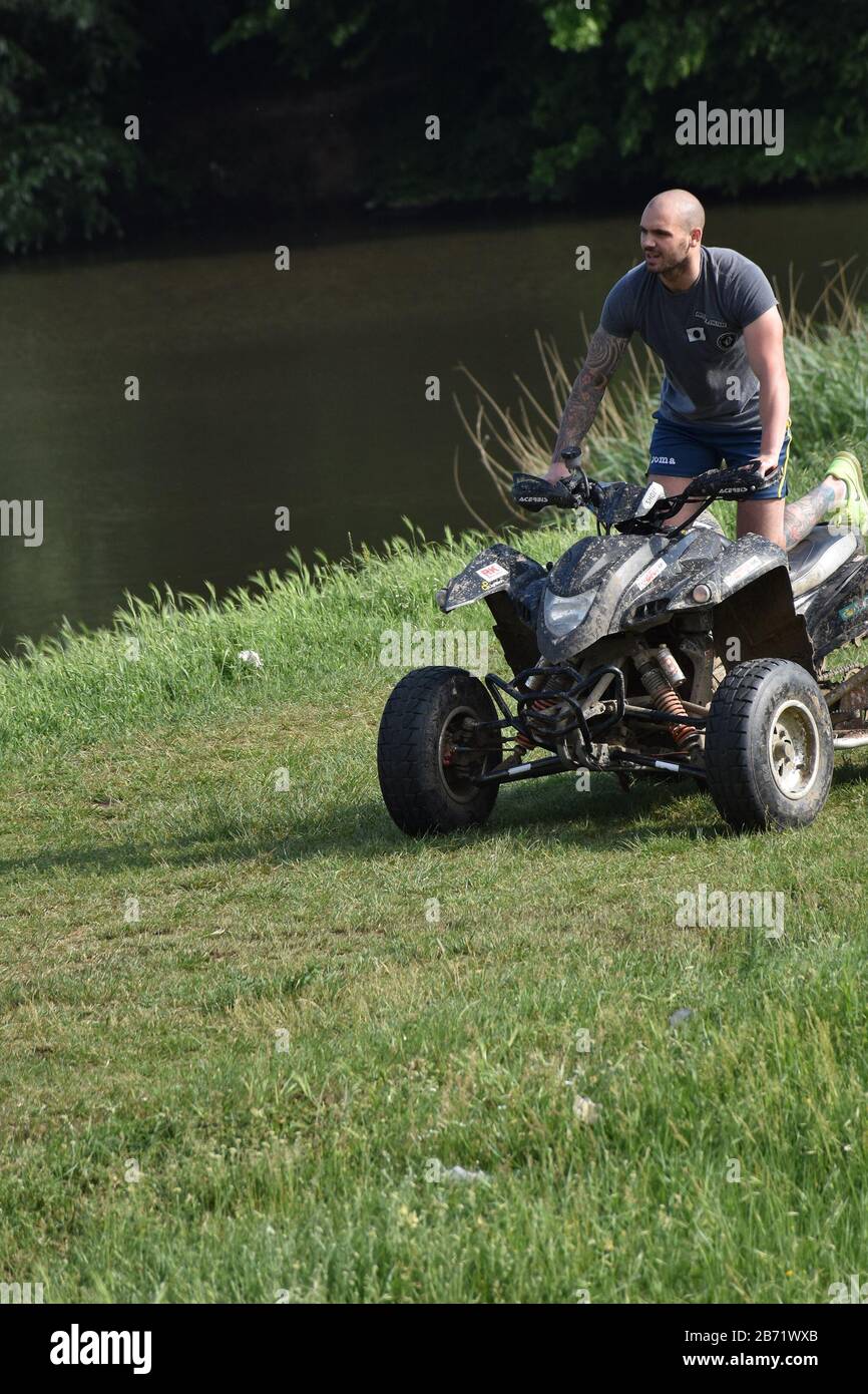Am grasbewachsenen Ufer des Flusses fährt ein Mann ein Quad Stockfoto