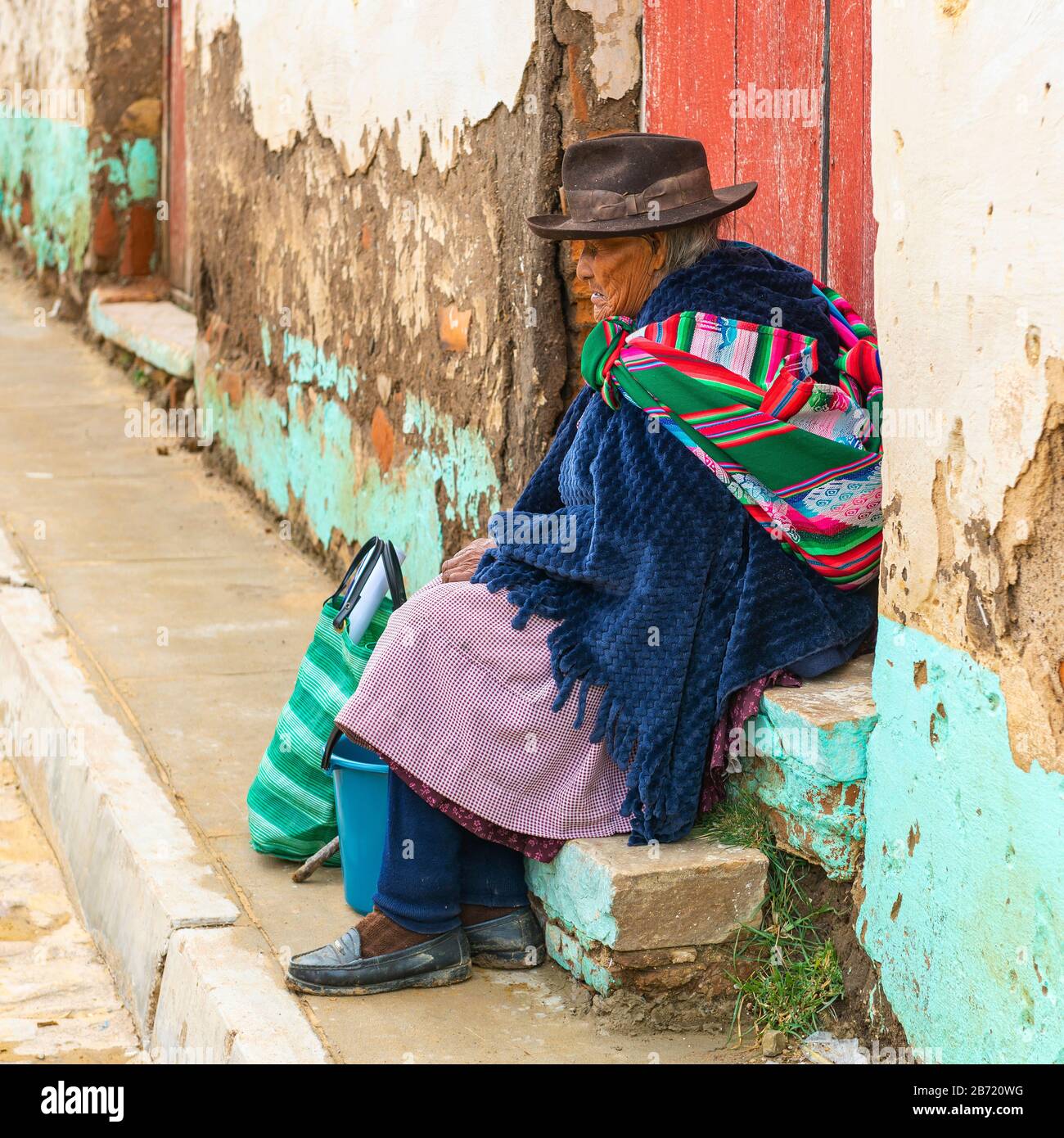 Indigene ältere Tarabuco-Frau am Bürgersteig in der Nähe des sonntagsmarktes mit traditionellem Hut und Textil in Tarabuco, Sucre Department, Bolivien. Stockfoto