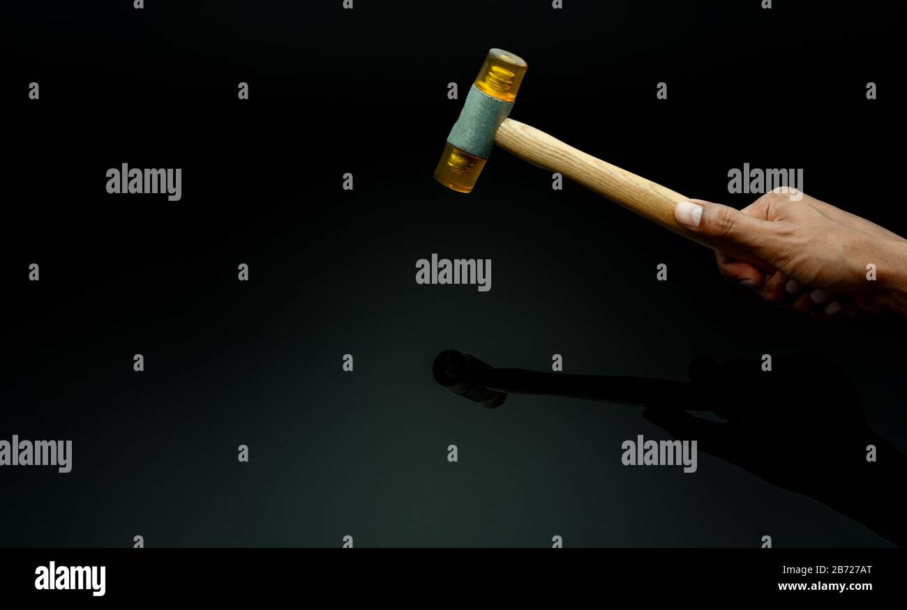 Hand des Mannes, der Kunststoffhammer isoliert auf dunklem Hintergrund hält. Holzgriff aus Kunststoffhammer für die Hand des männlichen Arbeiters. Hammerkopf aus weichem Material. Stockfoto