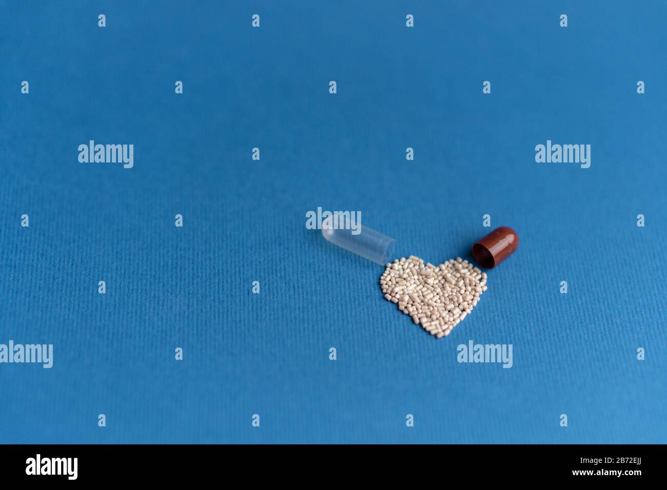 Granulat aus einer herzförmigen Kapsel auf klassischem blauem Grund gegossen. Herzförmige Medikamente. Herzsymbol durch Pillen gezeichnet. Stockfoto