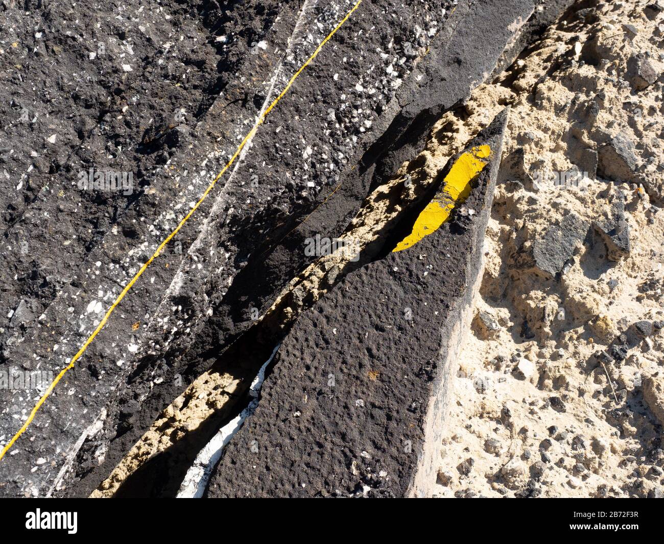 Asphaltrückstände auf der Straße, Nahbereich der zerbrochenen Asphaltpflasteroberfläche mit Fragment der bemalten gelben Linie, Asphaltschutt, Asphaltschutt und Asphaltschutt Stockfoto