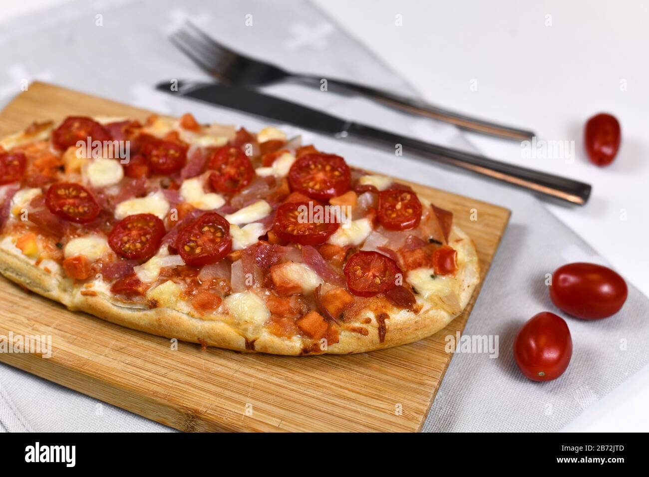 Hausgemachte, ovale Pizza mit Mozzarella-Käse, Tomaten- und Salami-Wurst auf Holzbrett Stockfoto
