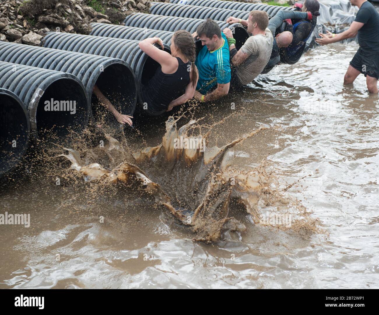 Tough Mudder Hindernislauf: Teilnehmer, die das Shawshanked Hindernis in kaltes schlammiges Wasser stürzen Stockfoto