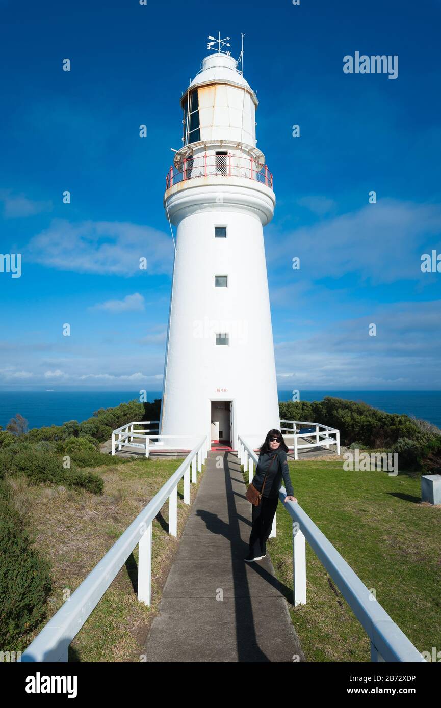 Blick auf den Cape Otway Lighthouse in Victoria, Australien als weibliche Touristin, posiert humorvoll auf die Leitplanken, die direkt zur Tür führen. Stockfoto