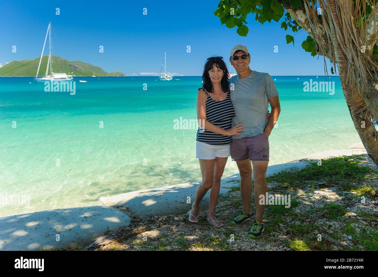 Ein Paar mit Blick auf die Kamera am Strand unter dem Baum im Fitzroy Island Resort in Queensland, Australien. Stockfoto