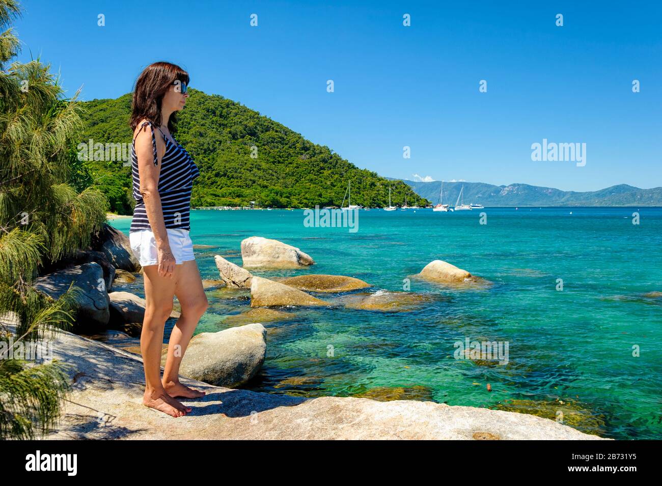 Weiblicher Tourist an einer felsigen Küste auf Fitzroy Island, in Australien, mit Blick auf das schöne türkisfarbene Wasser des Pazifischen Ozeans. Stockfoto