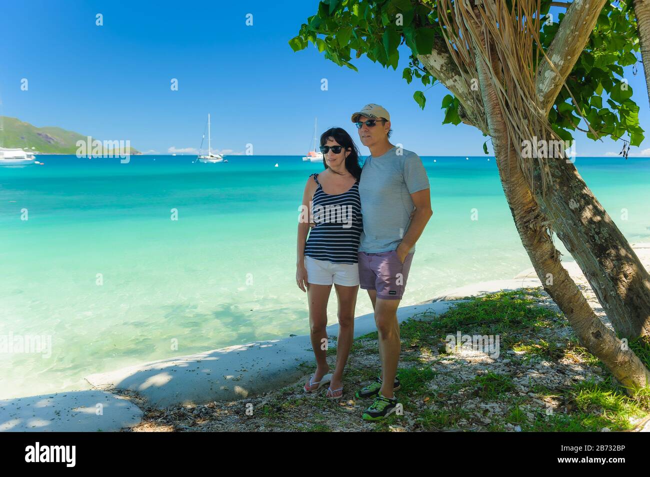 Ein Paar, das sich unter einem Baum umarmt und einen Strand auf dem Fitzroy Island Resort in Queensland, Australien, hinunterblickt. Stockfoto