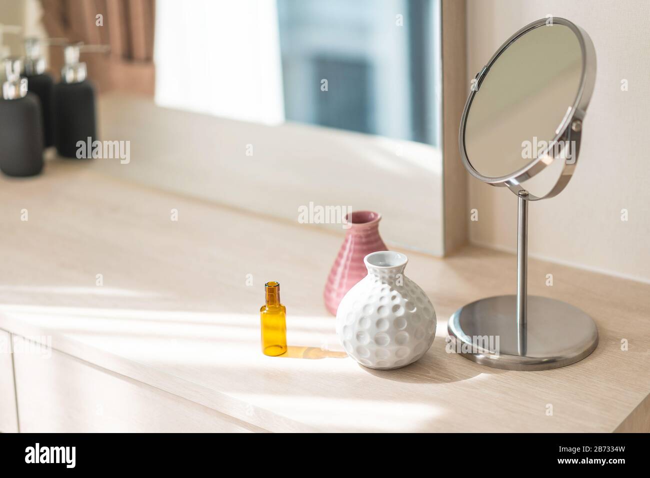 Abziehtisch mit Kreisspiegel, kleine Blumenvase in glänzendem Keramikweiß und rosafarbener Vase und Reagenzflasche auf der Holzkitze. Stockfoto