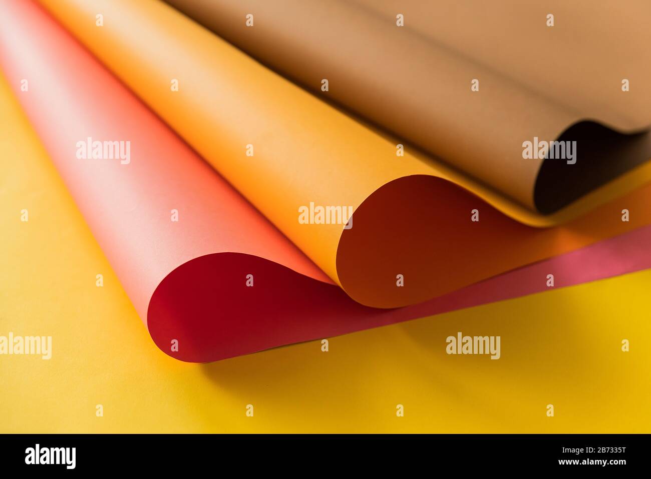 Rosafarbene und orangefarbene Papiere, die über gelbem Farbpapier zusammengerollt sind. Papiere für kreatives Handwerk und Design in der Schule. Stockfoto