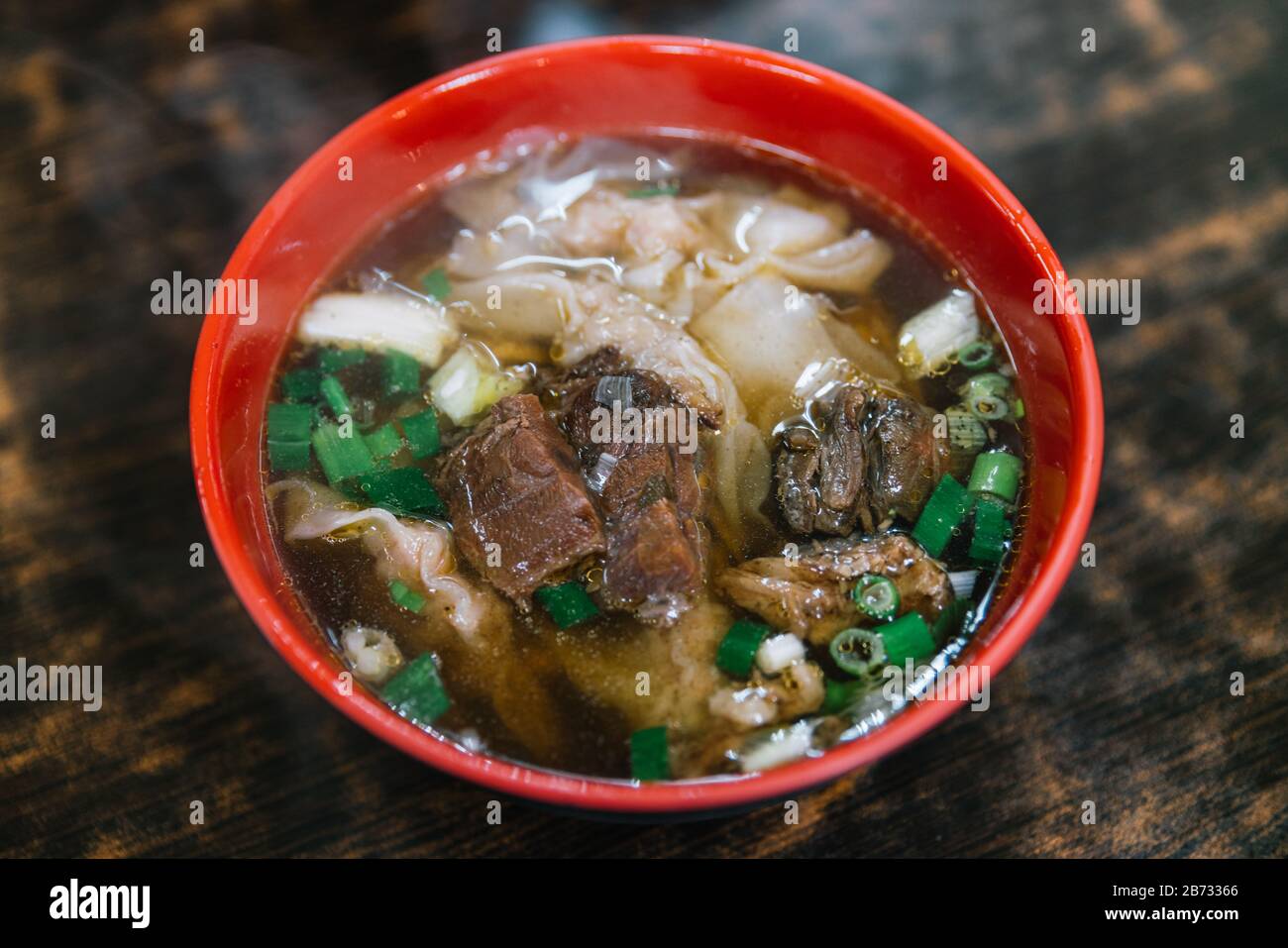 Nahaufnahme Taiwanesischer Art handgemauter Nudel mit gedämpftem Rindereintopf und wundersamen Suppen in roter, schwarzer Schüssel, berühmter Straßennahrung in Jiufen, Taiwan. Stockfoto