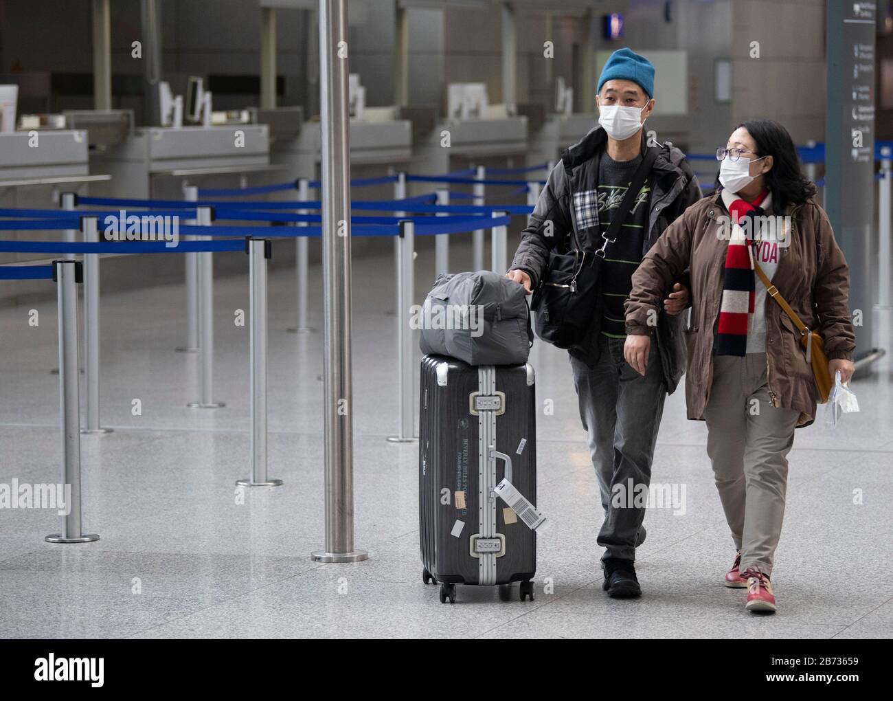 Flughafen Frankfurt, Deutschland. März 2020. 13. März 2020, Hessen, Frankfurt am Main: Masken schützen zwei Passagiere auf dem Weg durch das Terminal. Ab Samstag gilt für die Europäer ein Einreiseverbot in die USA. Auch die Luftfahrtindustrie war von den Reisebeschränkungen infolge der Corona-Pandemie betroffen. Allein die Lufthansa hat bis April bereits mehr als 20.000 Flüge gestrichen. Foto: Boris Roessler / dpa Credit: Dpa Picture Alliance / Alamy Live News Stockfoto