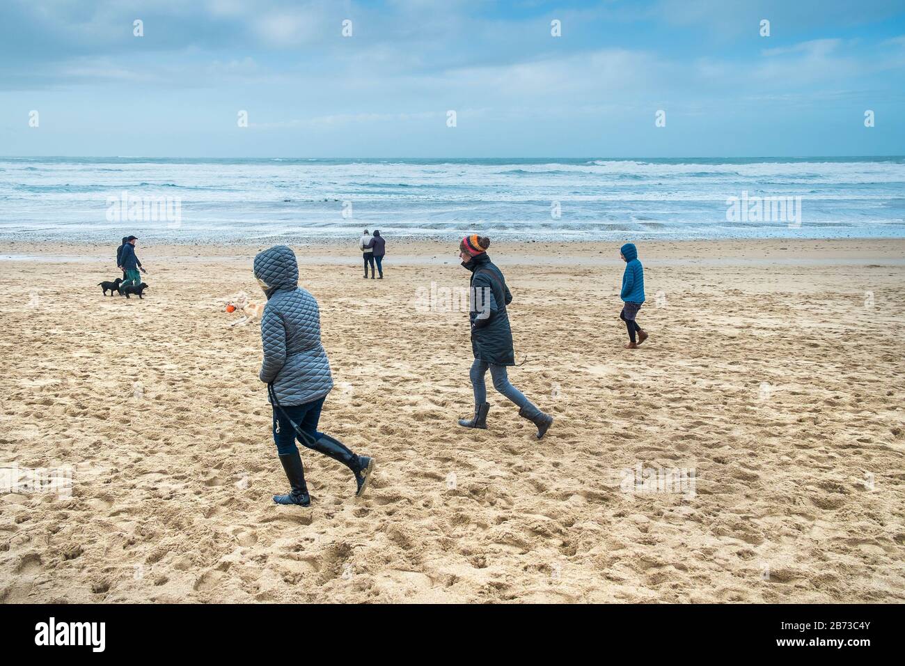 Menschen, die einen zügigen Spaziergang genießen, trotz der kalten, eisigen Witterungsbedingungen am Fistral Beach in Newquay in Cornwall. Stockfoto