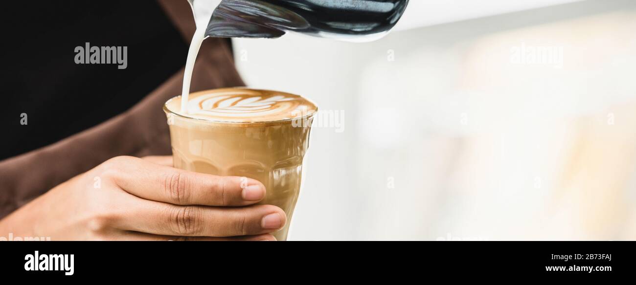 Banner des professionellen Barista, der gedämpfte Milch in eine Tasse aus Kaffeeglas gießt, um das schöne Latte Art Rosetta-Muster zu machen Stockfoto