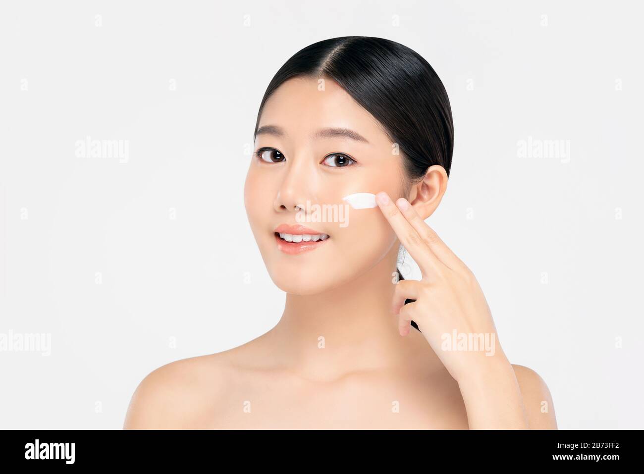 Junge, schöne asiatische Frau mit frischen, sauberen Aussehen, die Creme auf ein Gesicht auftragen, das auf weißem Hintergrund für Schönheits- und Hautpflegekonzepte isoliert ist Stockfoto