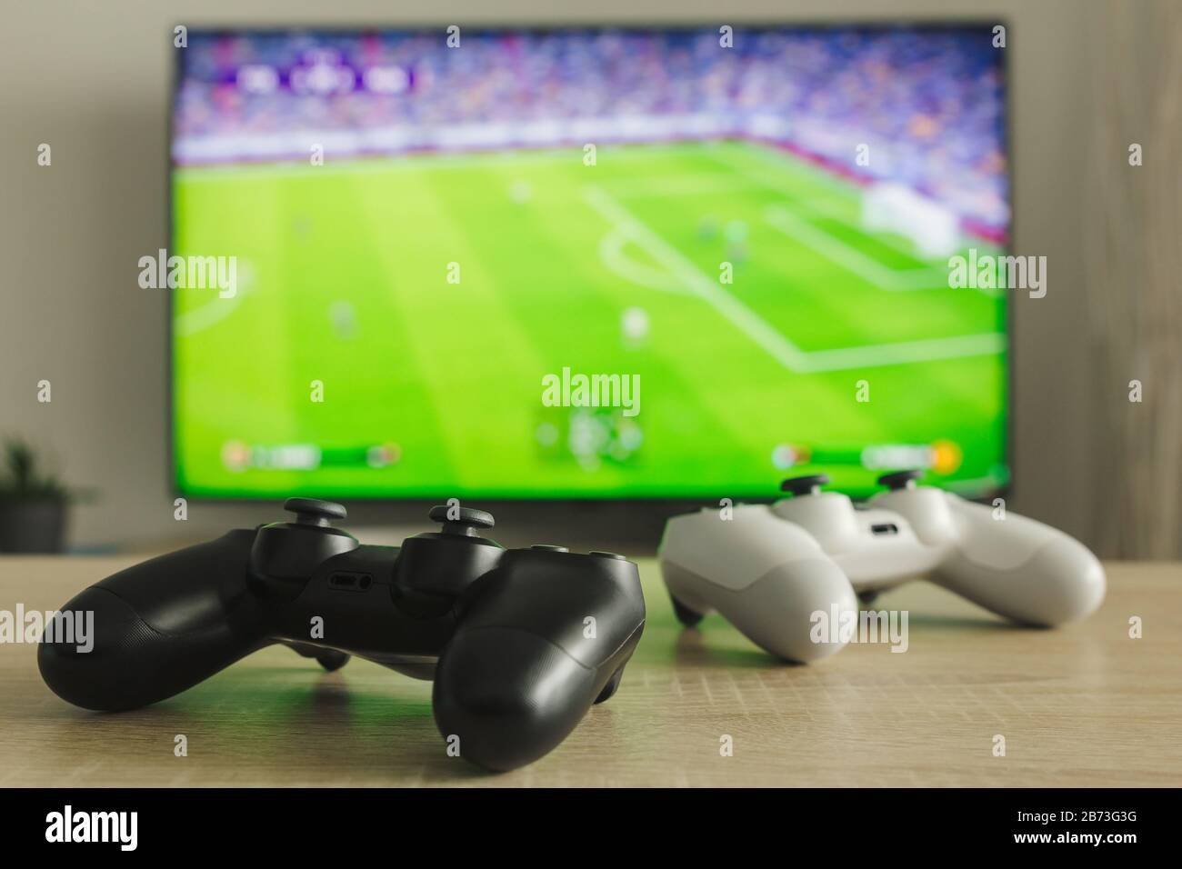 Stock-Foto von zwei Gamepads auf einem Tisch und einem Fußballspiel im Fernsehen im Hintergrund Stockfoto