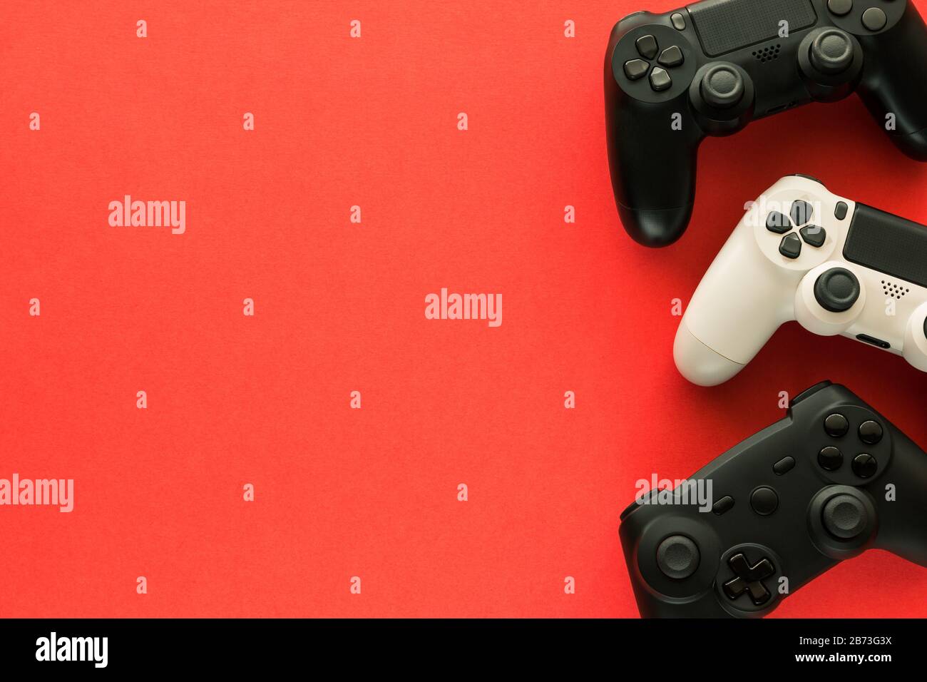 Stock-Foto von drei Gamepads auf rotem Hintergrund und Kopierbereich auf der linken Seite Stockfoto