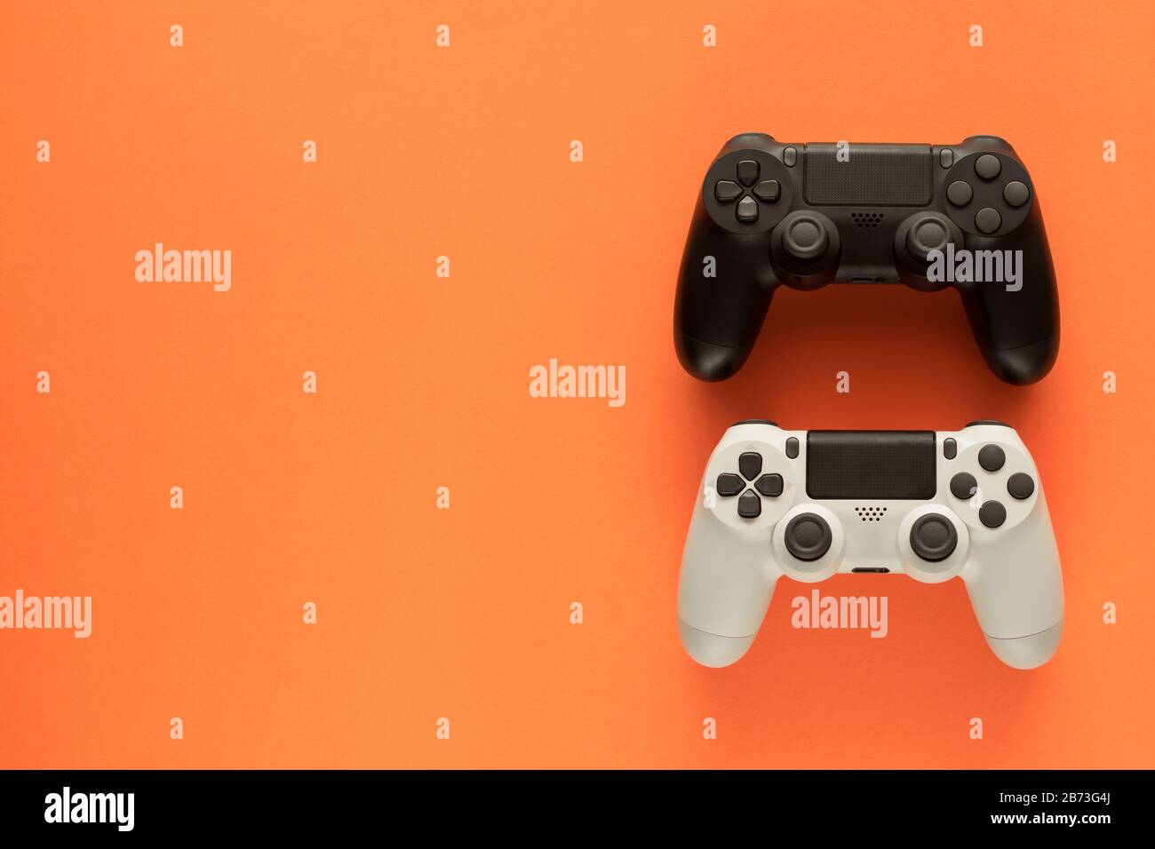 Stock-Foto von zwei Gamepads auf orangefarbenem Hintergrund und Kopierbereich auf der linken Seite Stockfoto