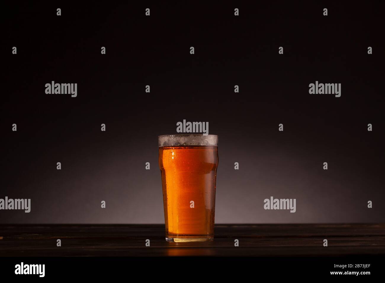 "Pint of Beer still Life"-Einrichtung mit dunklem Tisch und minimaler Beleuchtung. Dunkler Hintergrund mit Kopierbereich und Textraum. Stockfoto