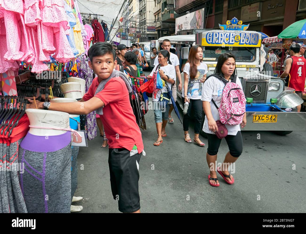 Divisoria Market, Manila, Philippinen: Kleiner Junge, der ein Bekleidungsgeschäft besucht, während Käufer neben einem philippinischen Jeepney laufen Stockfoto