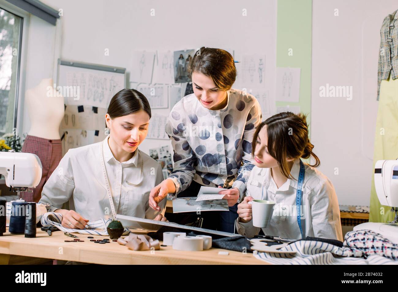 Modedesign, Kommode, maßgeschneidertes Konzept. Drei junge kaukasische Frauen arbeiten im hellen Atelier zusammen und bereiten neue handgefertigte cl vor Stockfoto