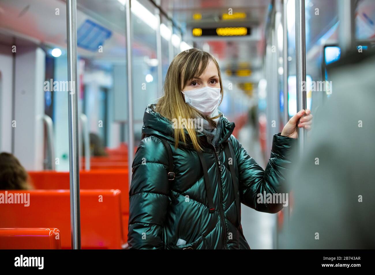 Frau im Winter Mantel mit Schutzmaske im Gesicht im U-Bahn-Auto stehend, per Telefon, besorgt aussehend. Vorbeugende Maßnahmen an öffentlichen Orten Stockfoto