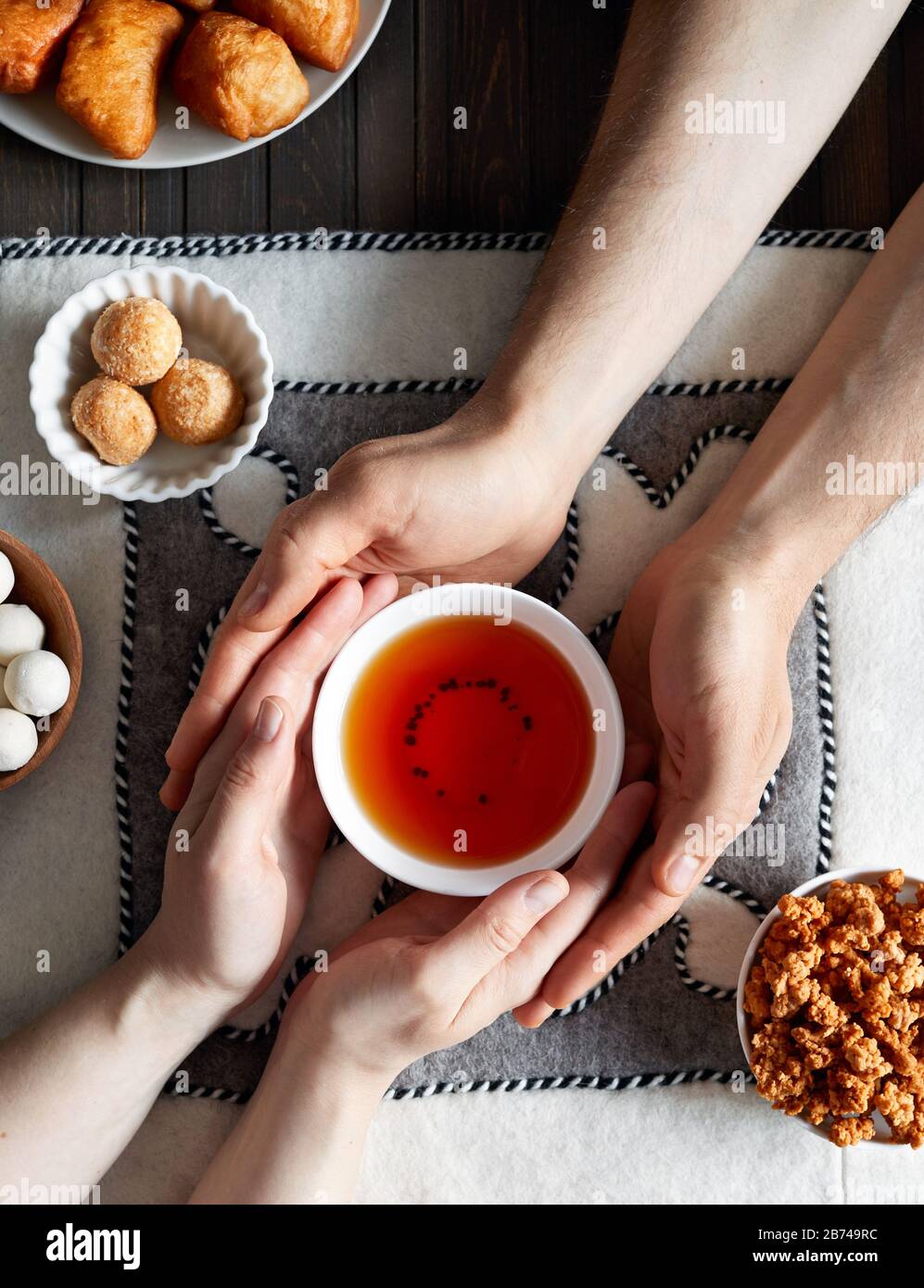 Kasachische Frau und Mann, die Teeschale mit schwarzem Tee in der Nähe von nationalen kasachischen Speisen wie Zhent, Baursak und kurt während Nauryz-Festival auf ethnischen Filzbacken halten Stockfoto