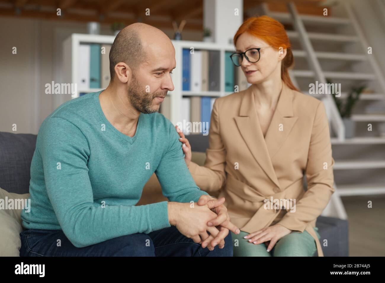 Trauriger reifer Mann, der zusammen mit der Frau auf dem Sofa sitzt und ihn bei seinem Besuch unterstützt Stockfoto